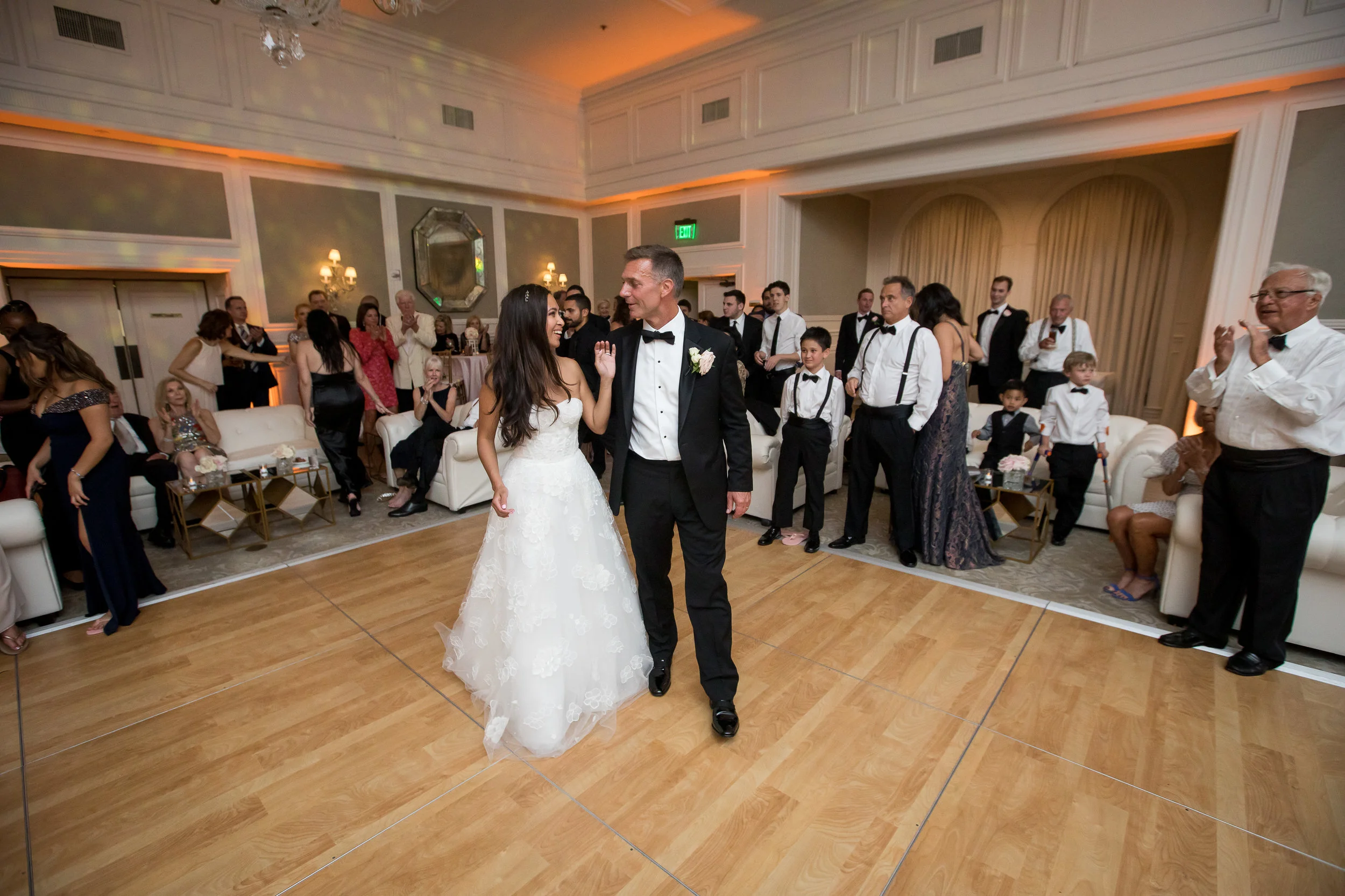 Bride and groom dancing at their wedding reception while guests watch and celebrate around them.