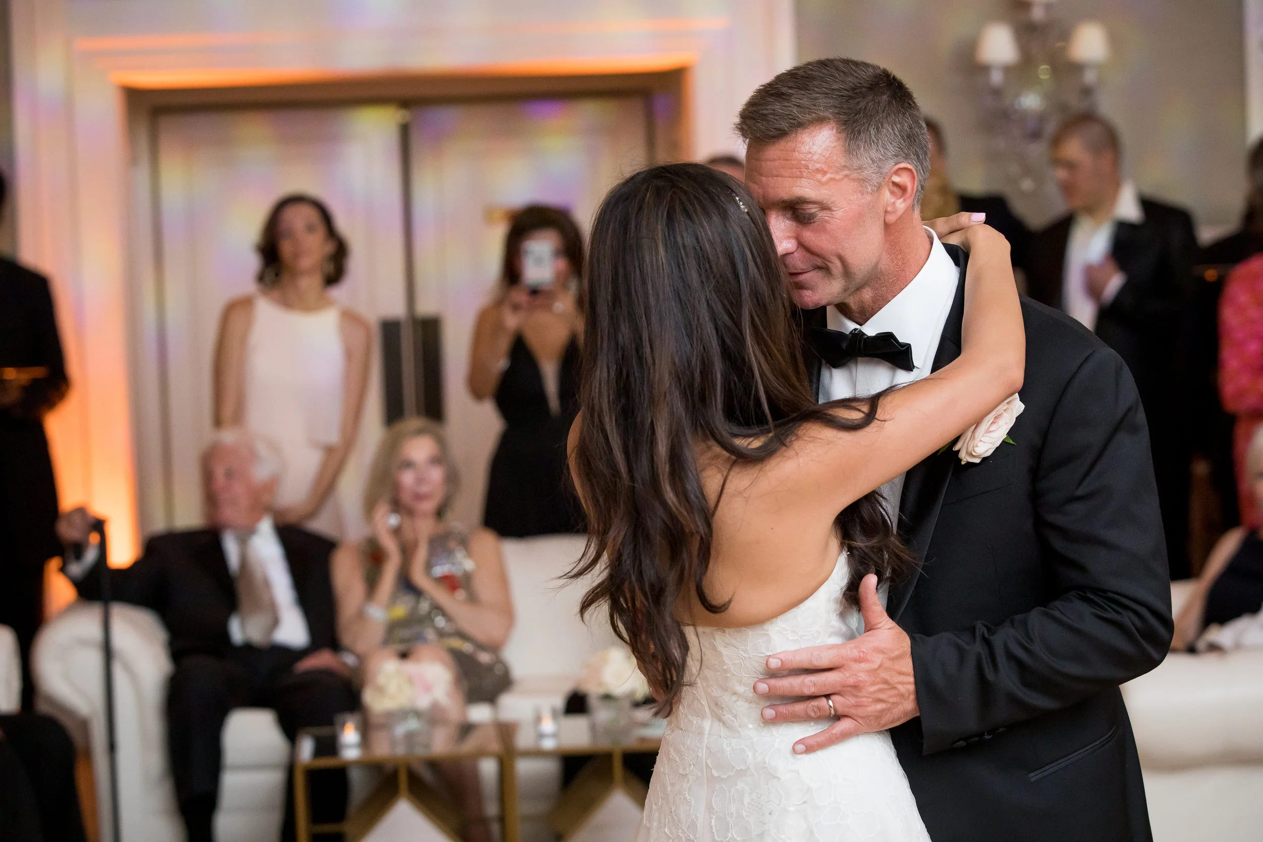 A couple sharing a first dance at a wedding reception, with guests watching in the background.