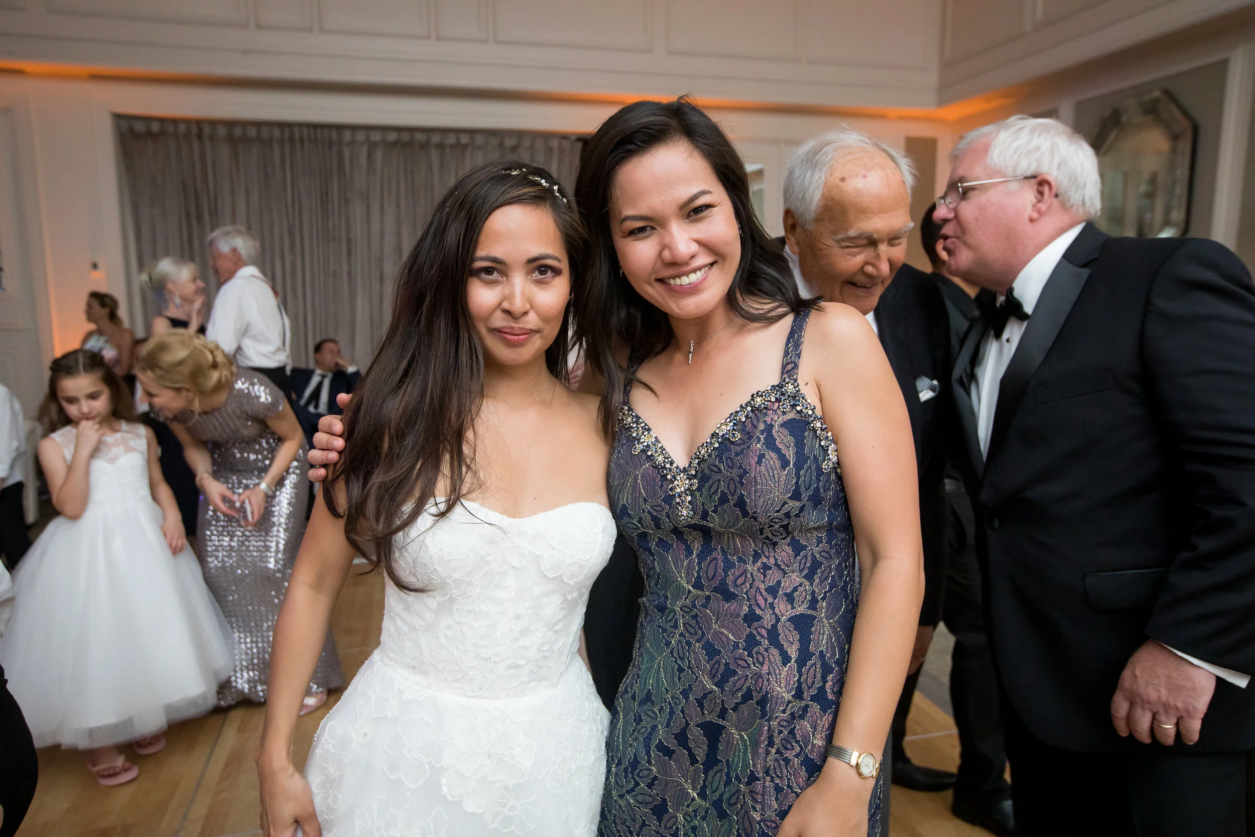 Two women at a formal event, smiling and posing for a photo. The woman on the left is wearing a white dress, and the woman on the right is wearing a dark patterned dress.