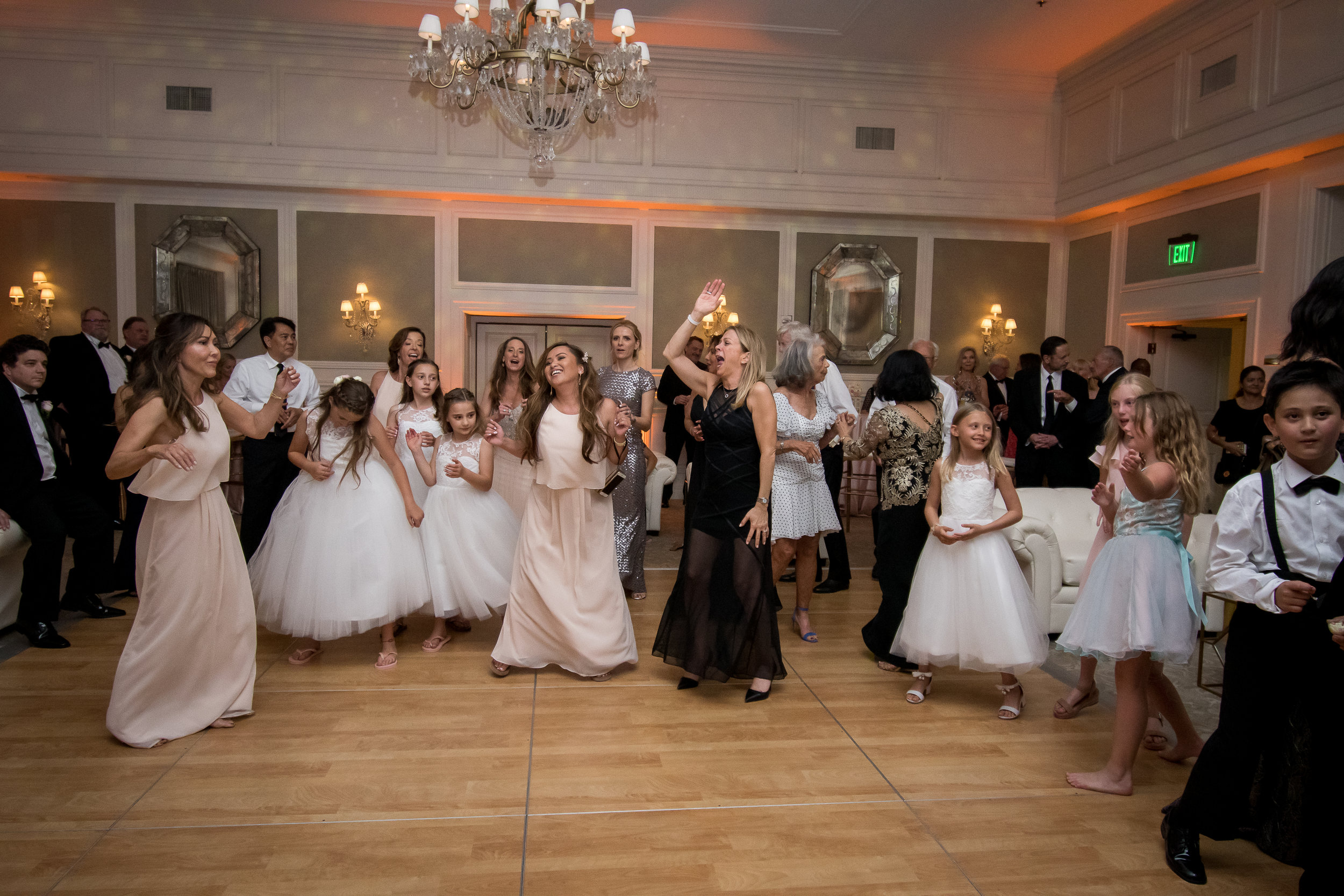 People dancing and socializing at a formal event in a decorated banquet hall with elegant lighting and wall mirrors.