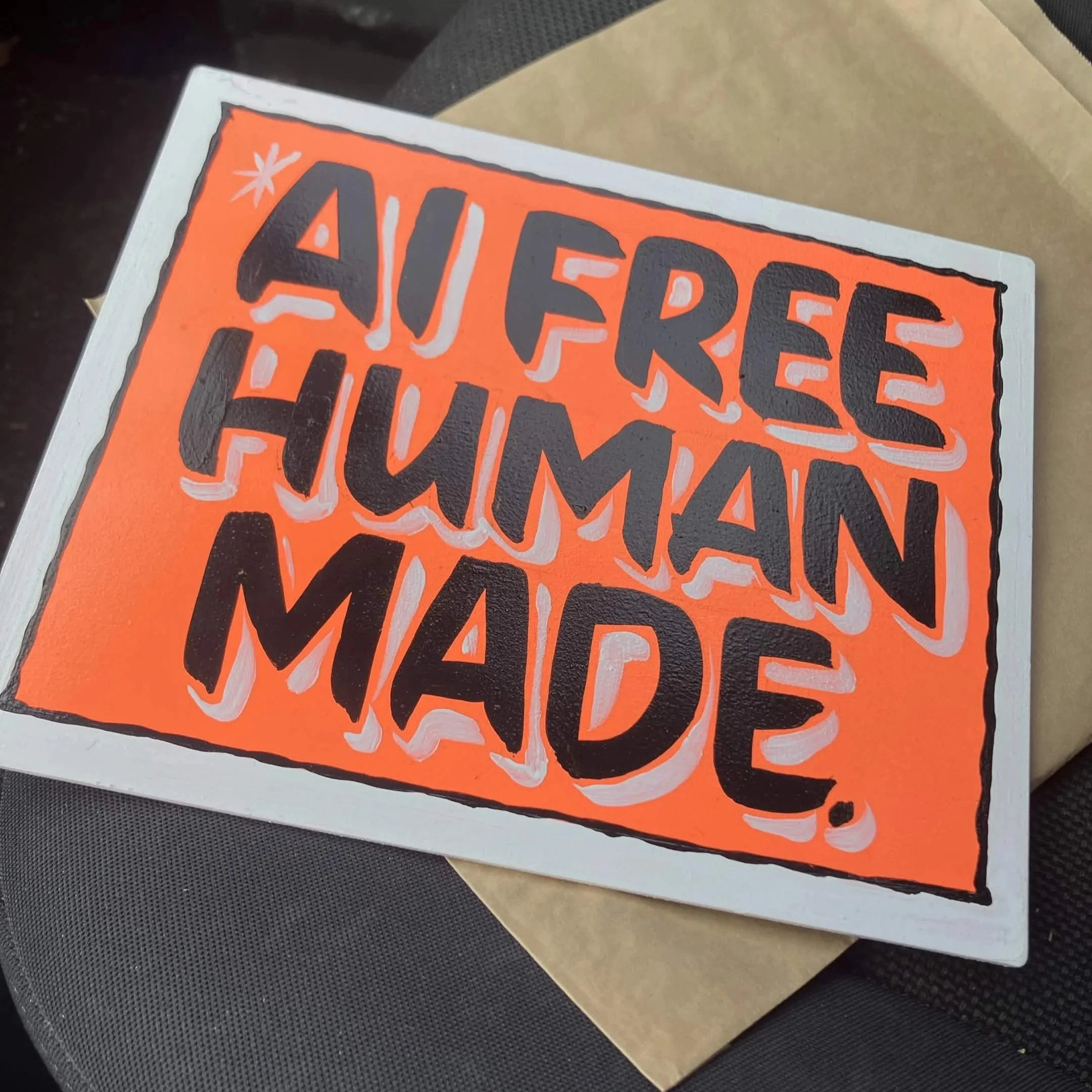 An handpainted sign that says "AI free. Human made." in black letters on an orange background