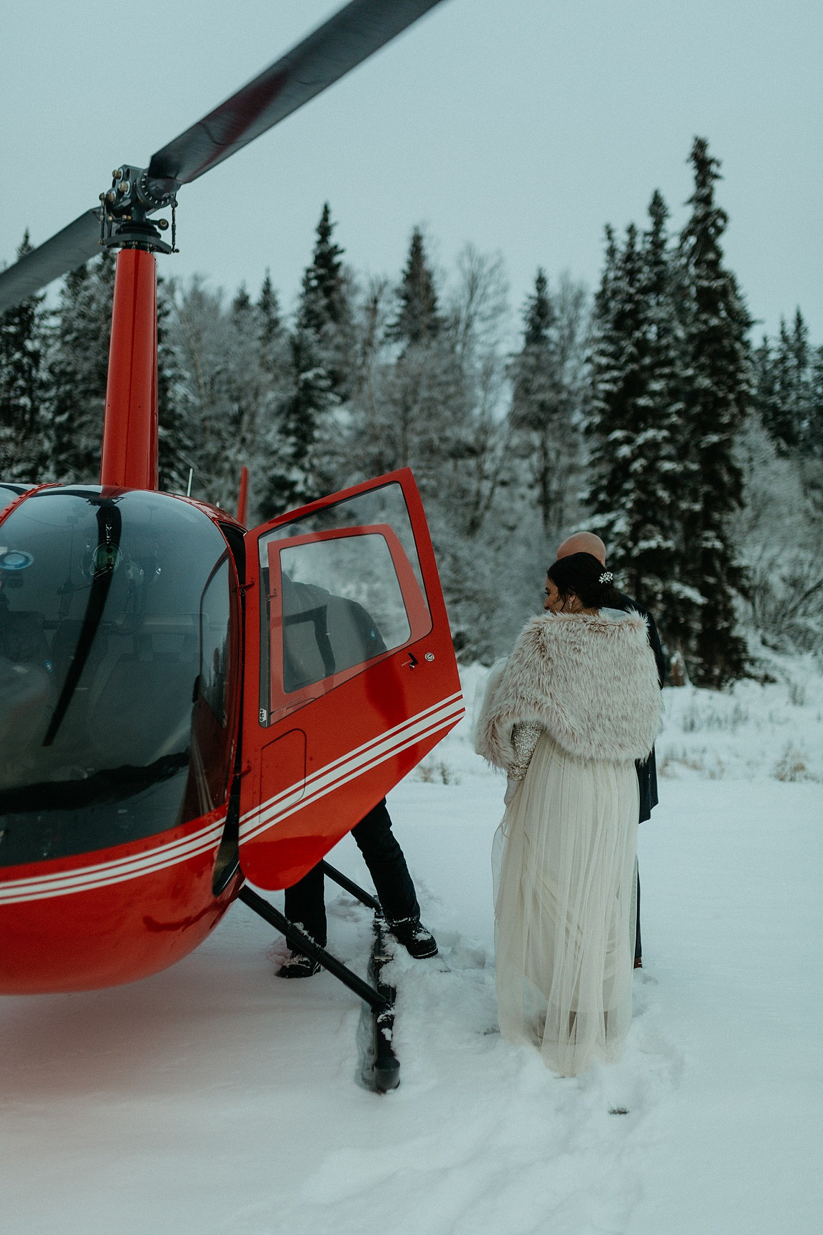  Bride and groom approaching a helicopter in the snow of Alaska  