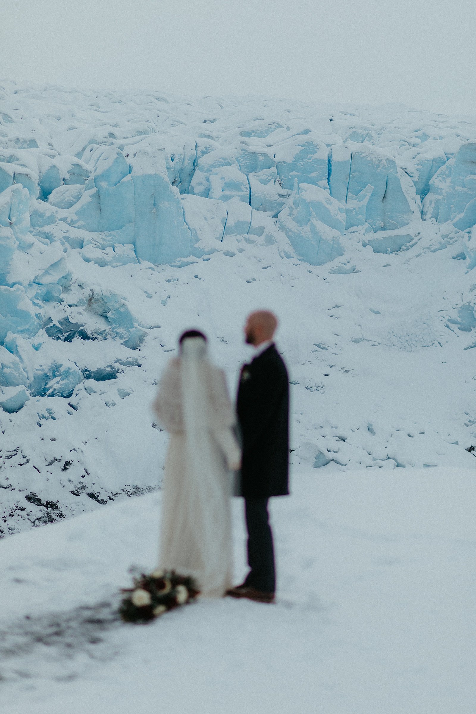  Bride and groom standing on a snowy plain for glacier adventure elopement 