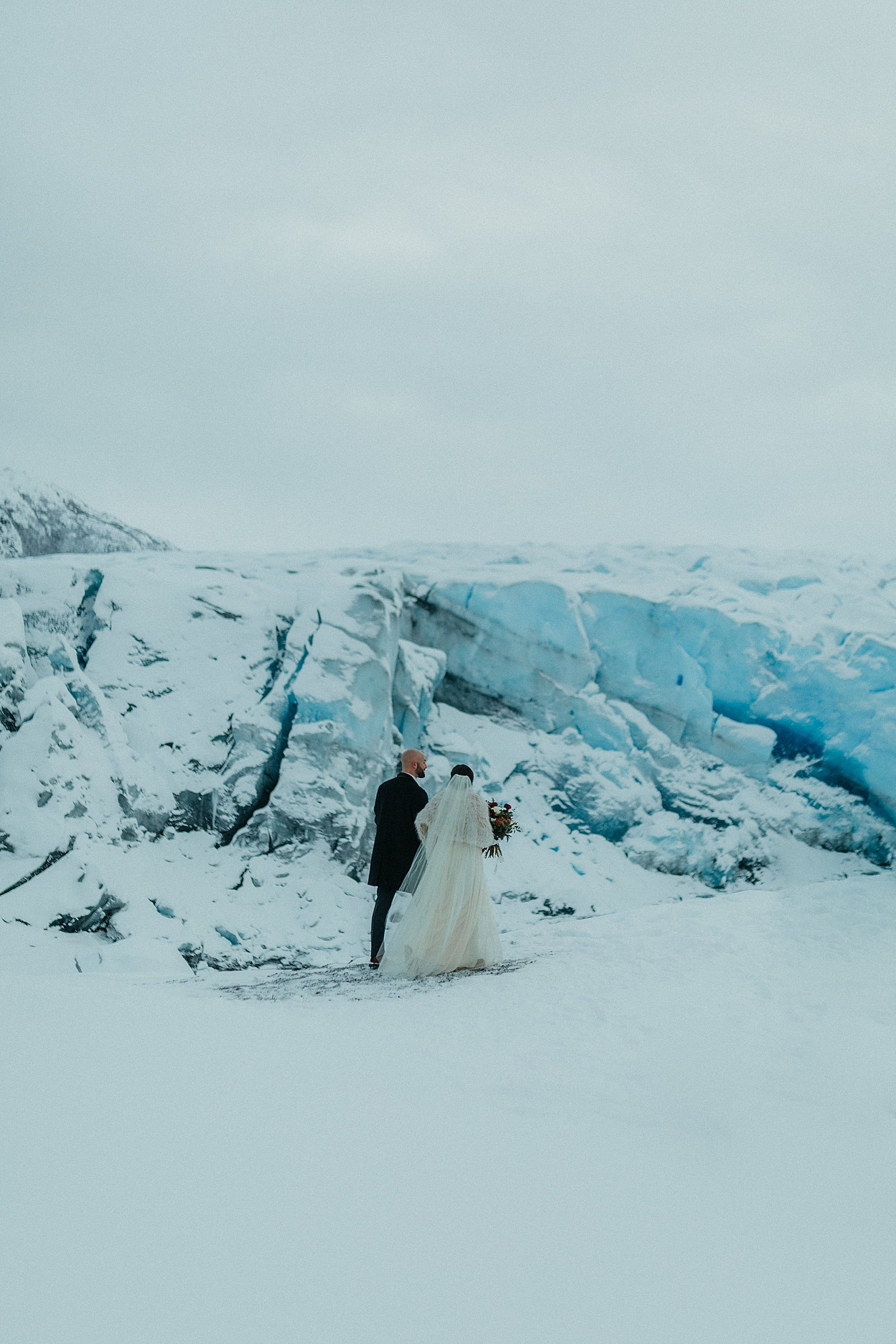  Bride and groom walking along a glacier after their intimate ceremony 