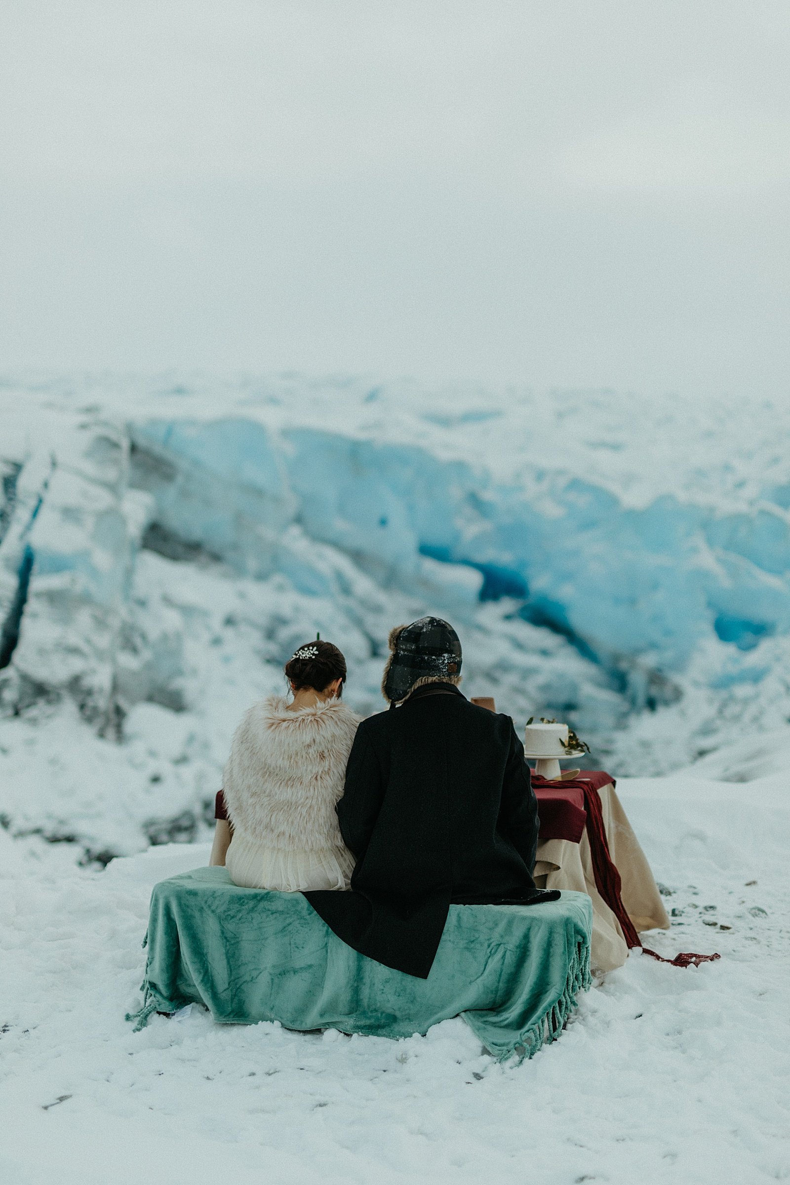  Bride and groom sitting at private table on a snowy mountain for glacier adventure elopement 