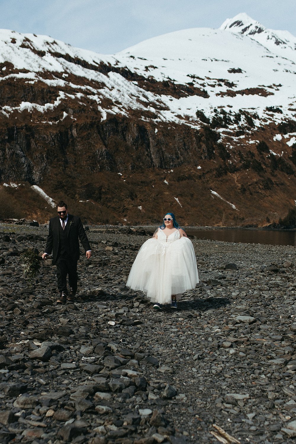 Bride and groom walking on a pebble shore with sunglasses on by Alaska Elopement Photographer 