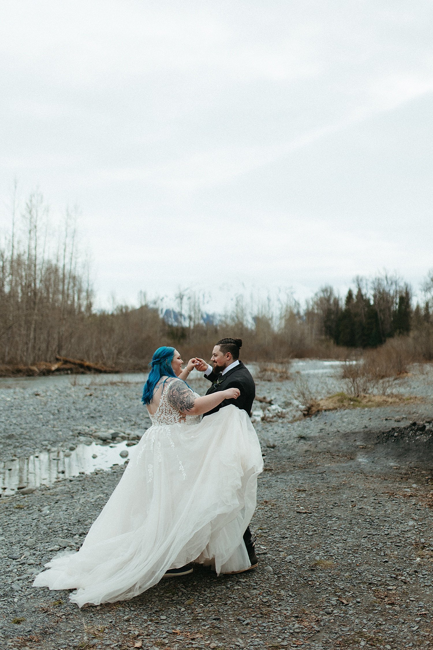  Bride with blue hair and groom dancing next to a creek by Alaska Elopement Photographer 