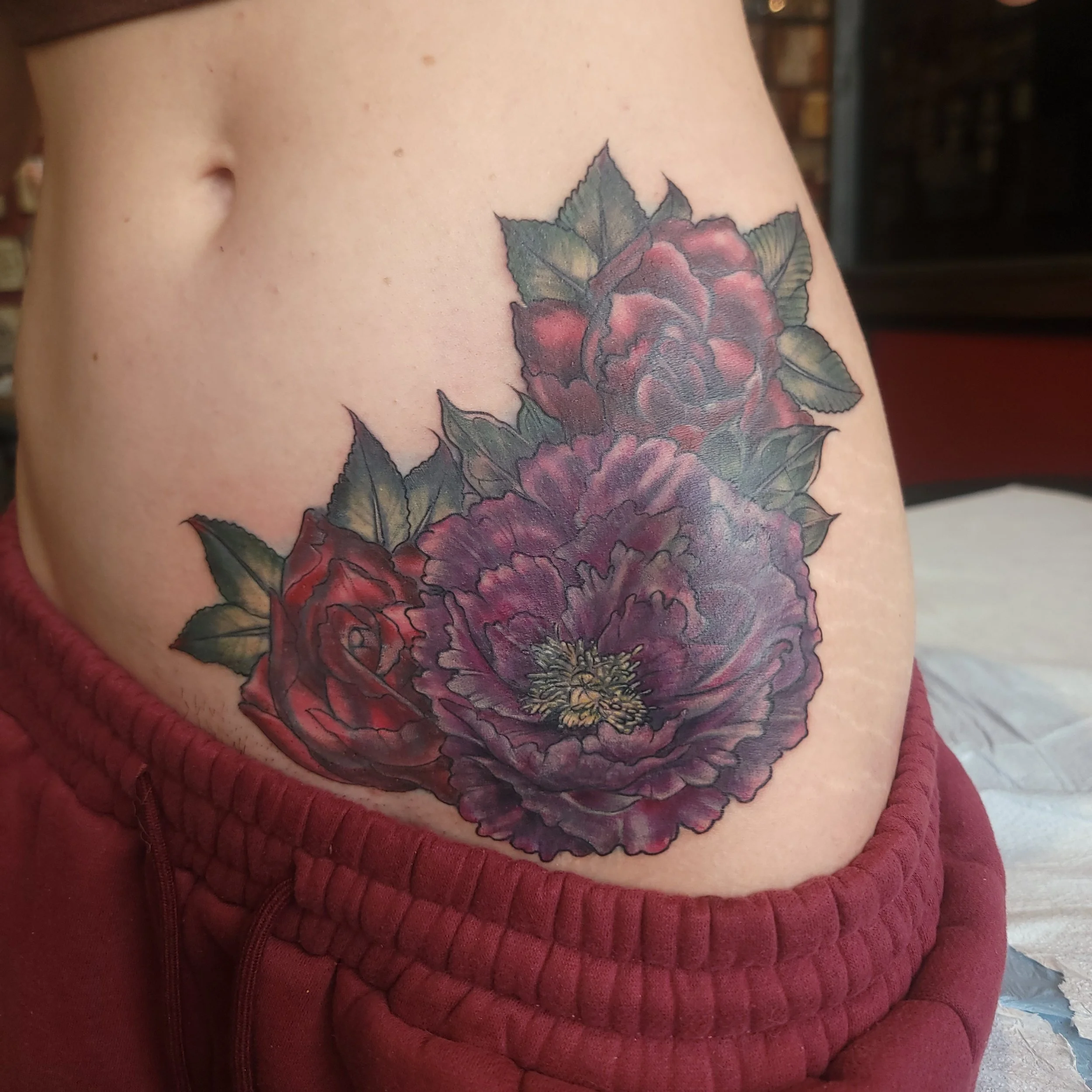 The after of the floral tattoo on a person's side, featuring red and purple flowers with green leaves. Coverup of a cheshire cat