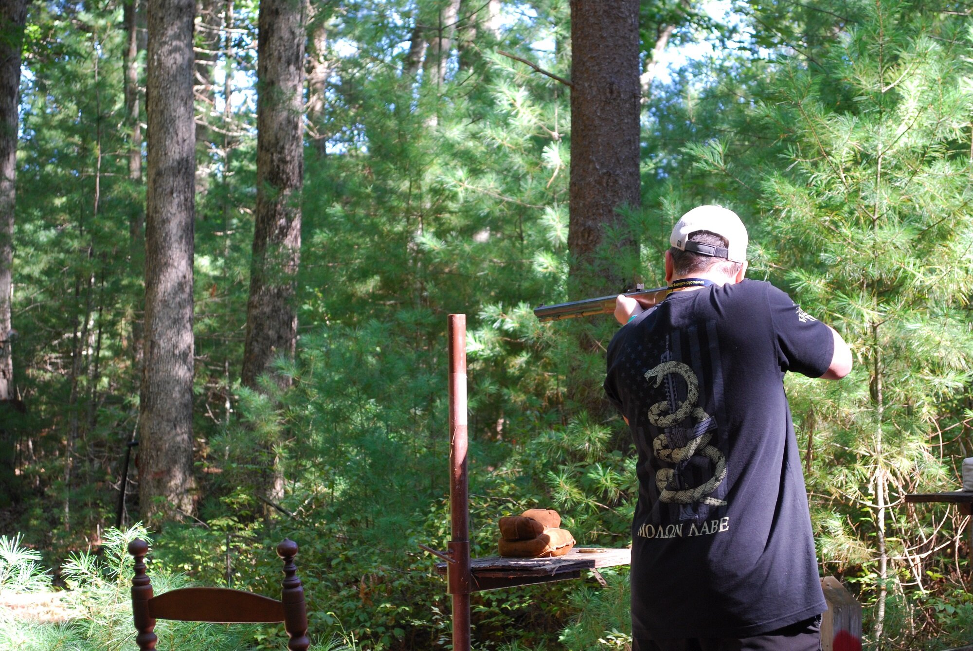 A man shooting a rifle in a forested area.