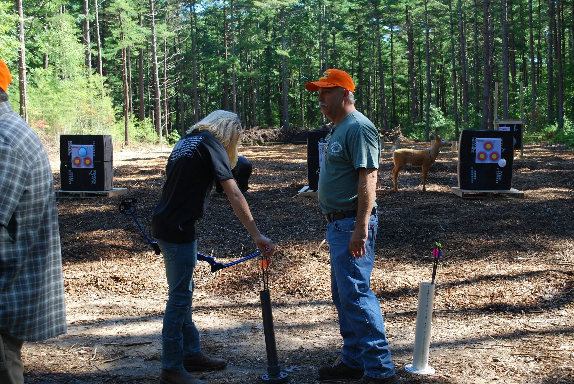 People participating in a archery activity in a forest clearing, with target boards and arrows set up in the background.
