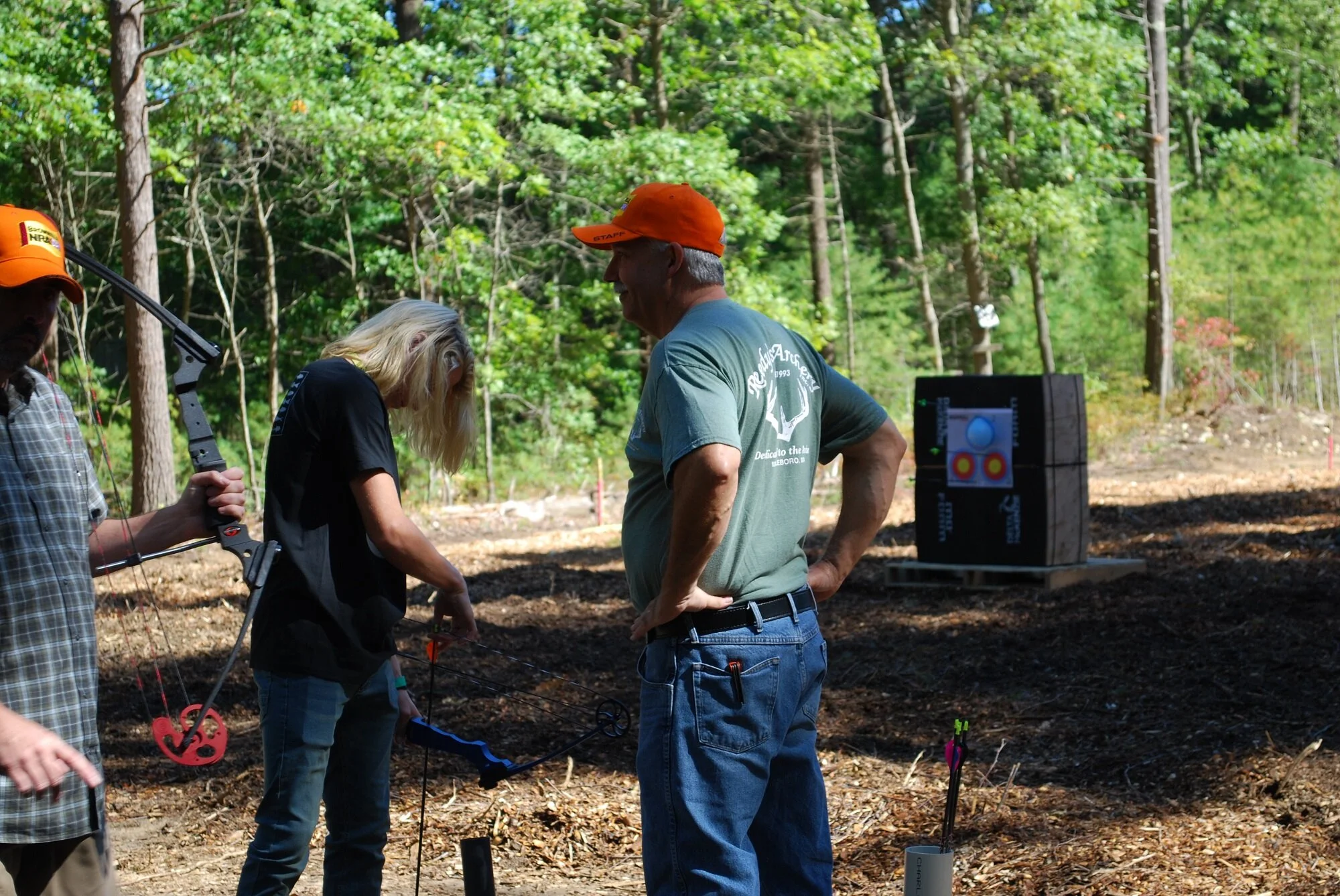 A group of people in a forest, with archery equipment, participating in an archery activity or competition.
