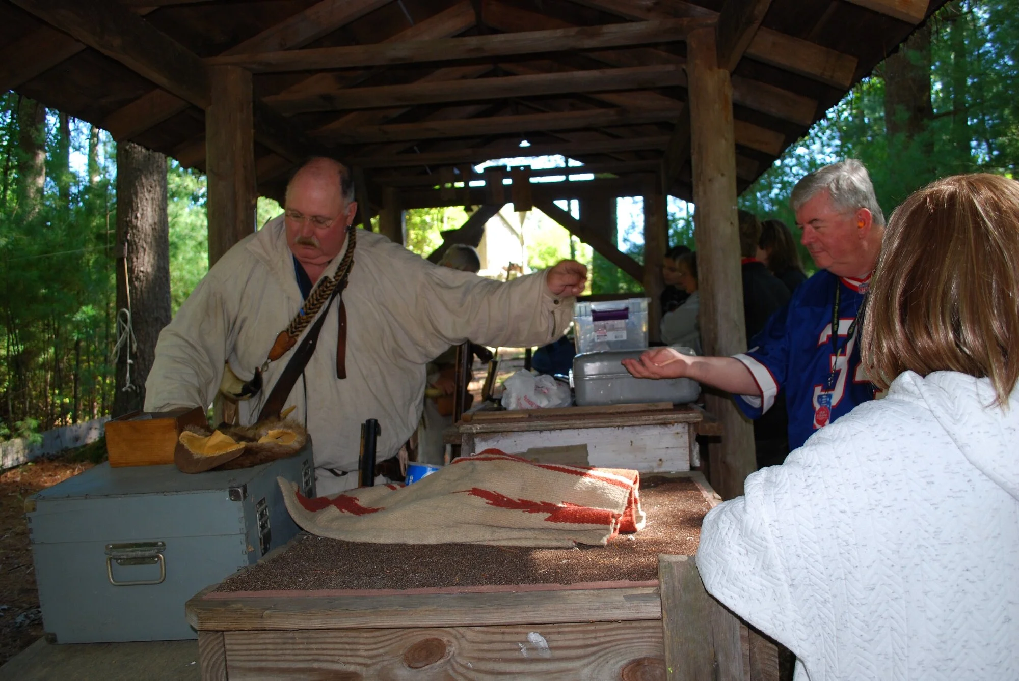 People gathered at an outdoor wooden pavilion, with one man receiving something from another man, amidst trees and natural surroundings.