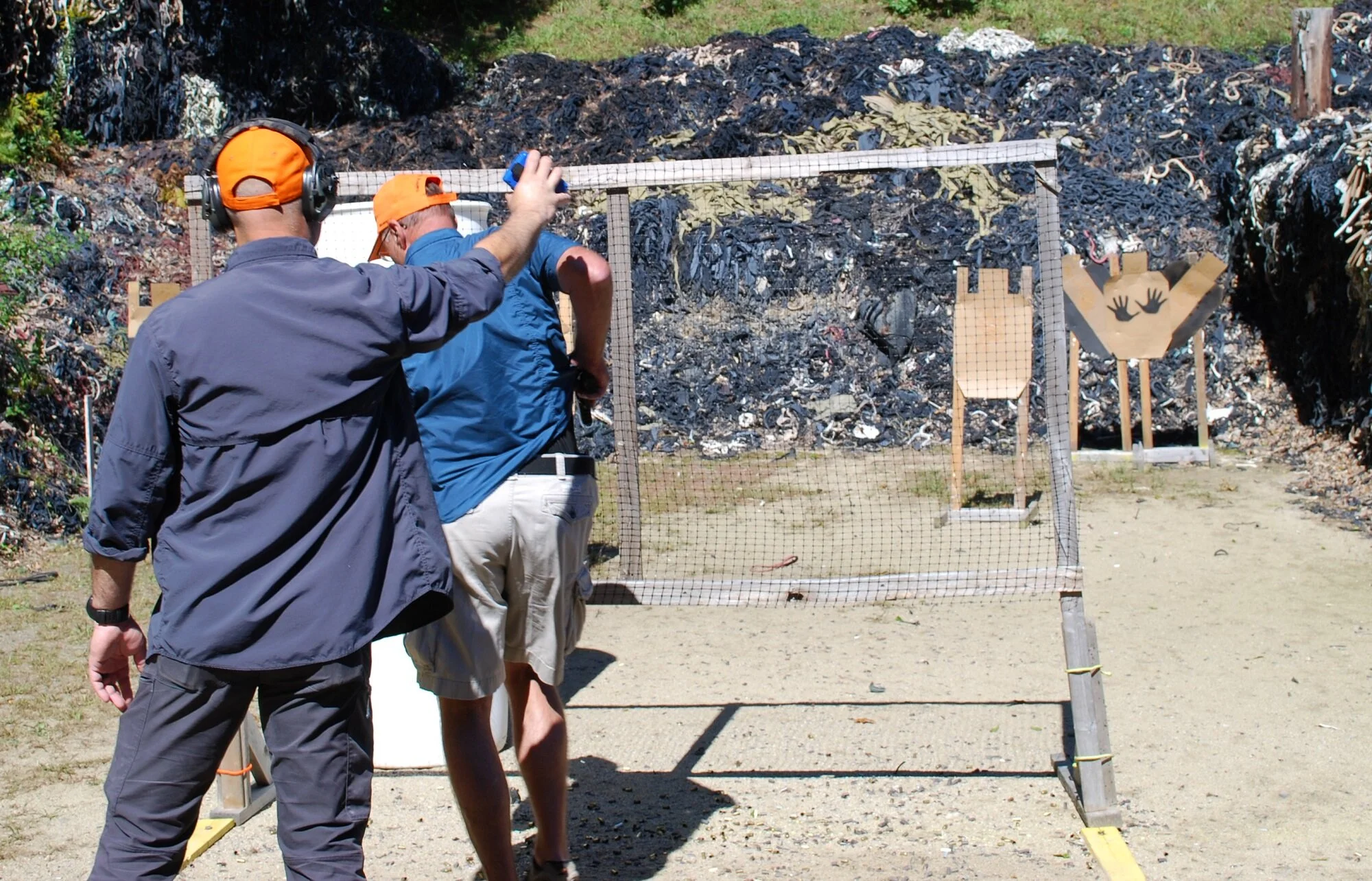 Two men standing at a shooting range with targets against a rocky background.
