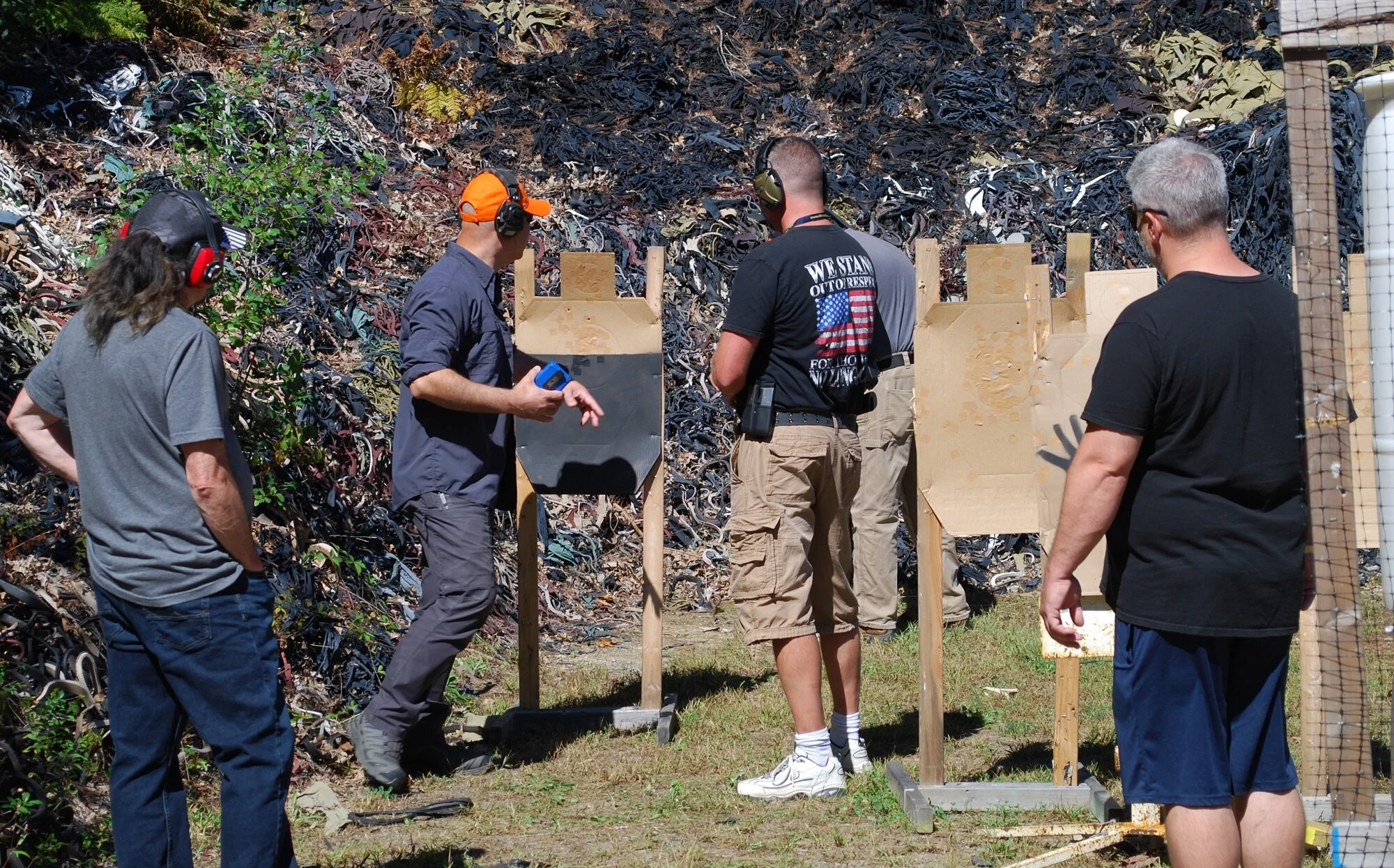 A group of five people at an outdoor shooting range with cardboard targets, ear protection.