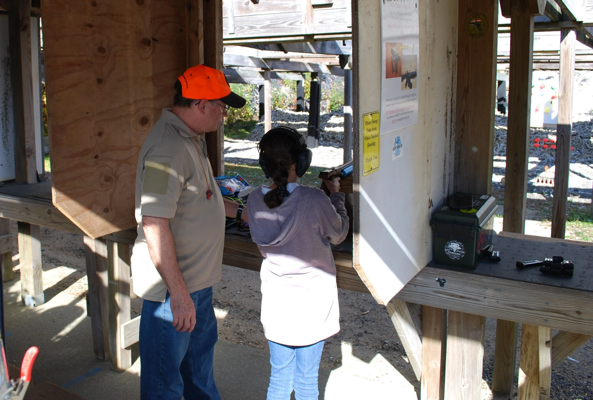 A man and a girl at a shooting range, with the girl aiming a handgun under supervision.