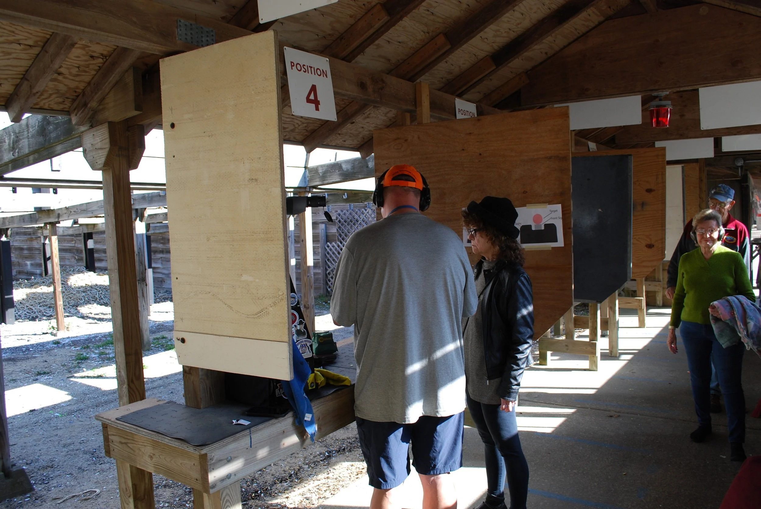 People at a shooting range, with a sign indicating 'Position 4' for a shooting station, and targets visible in the background.