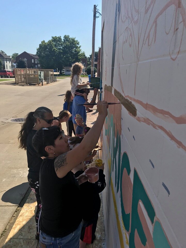  Vermillionaires make the stretch to reach higher parts of the design during the community paint day.  