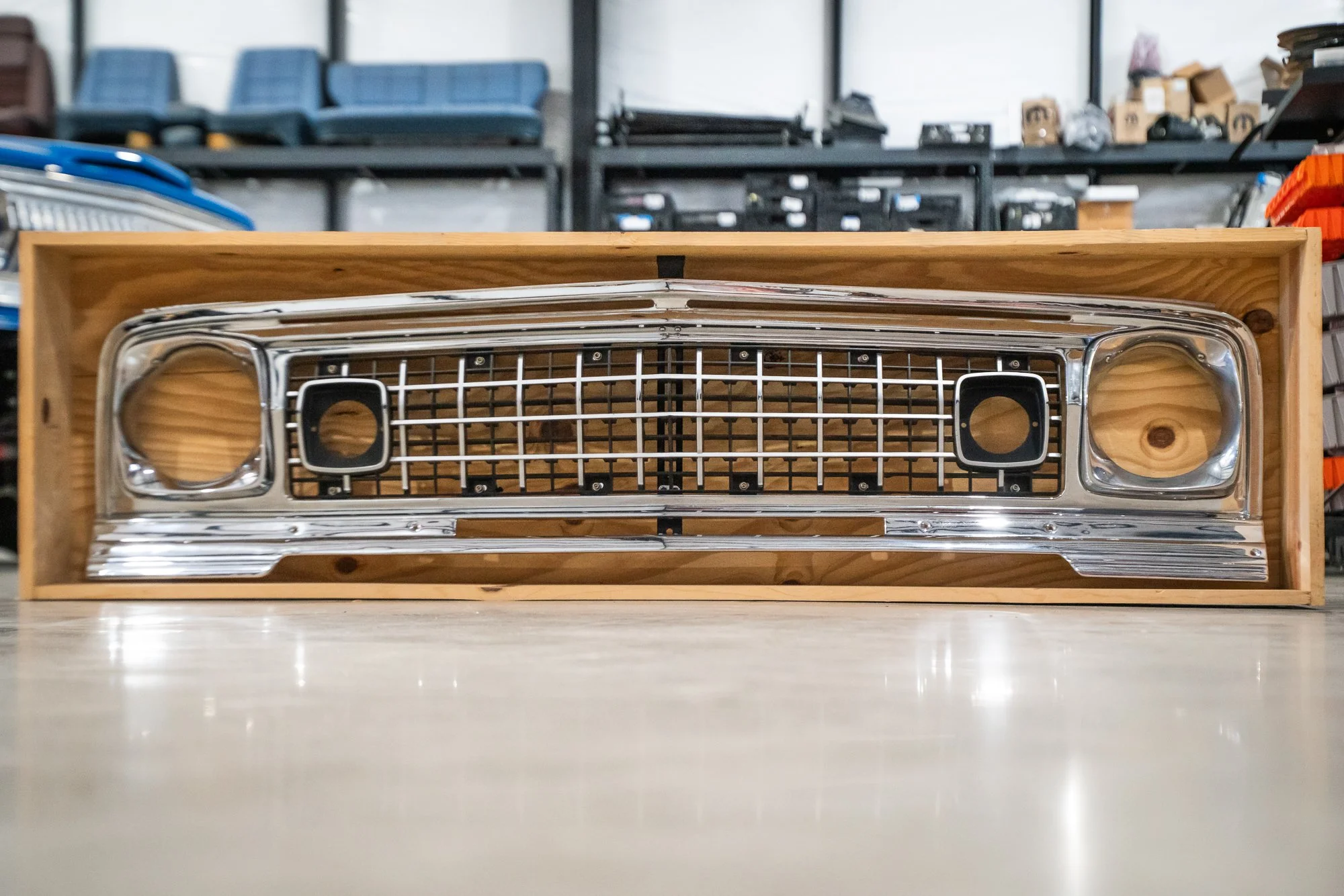 A car front grille with circular areas for headlights, placed inside a wooden box on a workshop floor.