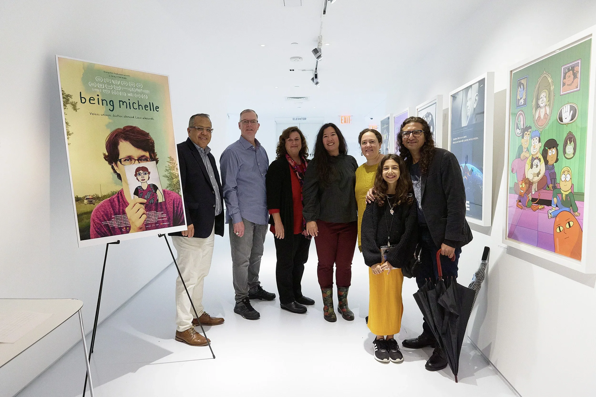 A group of eight people, including children, standing in an art gallery with colorful artwork displayed on the white walls.