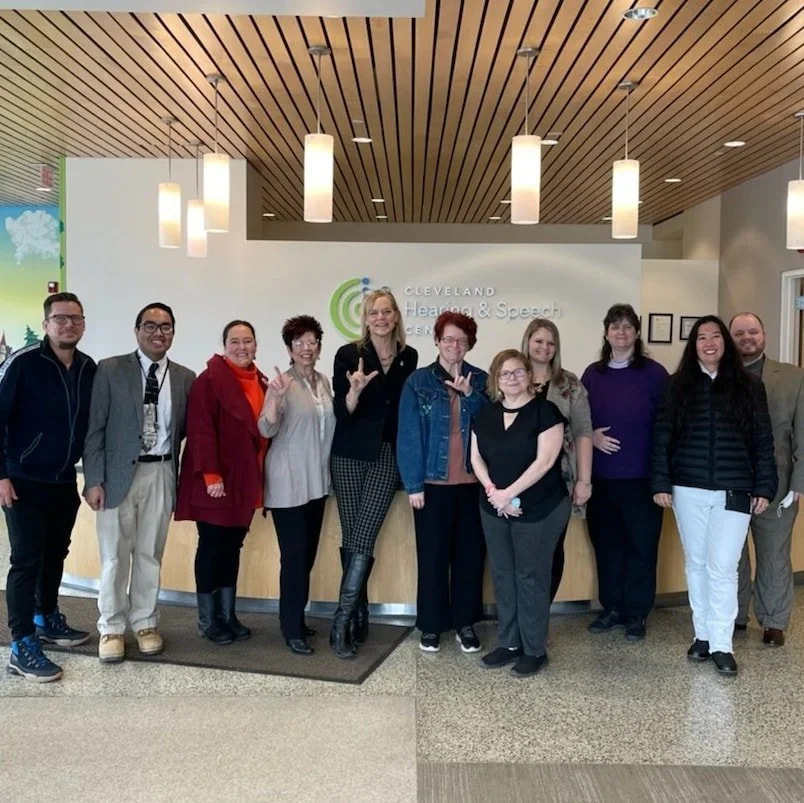 Group of ten people standing in front of a reception desk at Cleveland Hearing & Speech Center, smiling and posing for a photo.