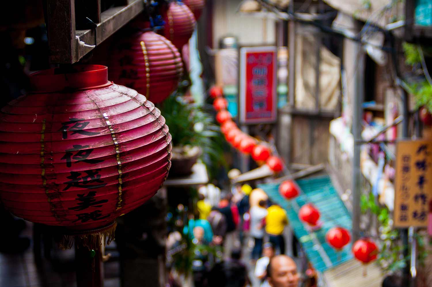 Chinese lanterns placed on walls and a blurry view below of people walking in a market road in jiufen old street (Copy)