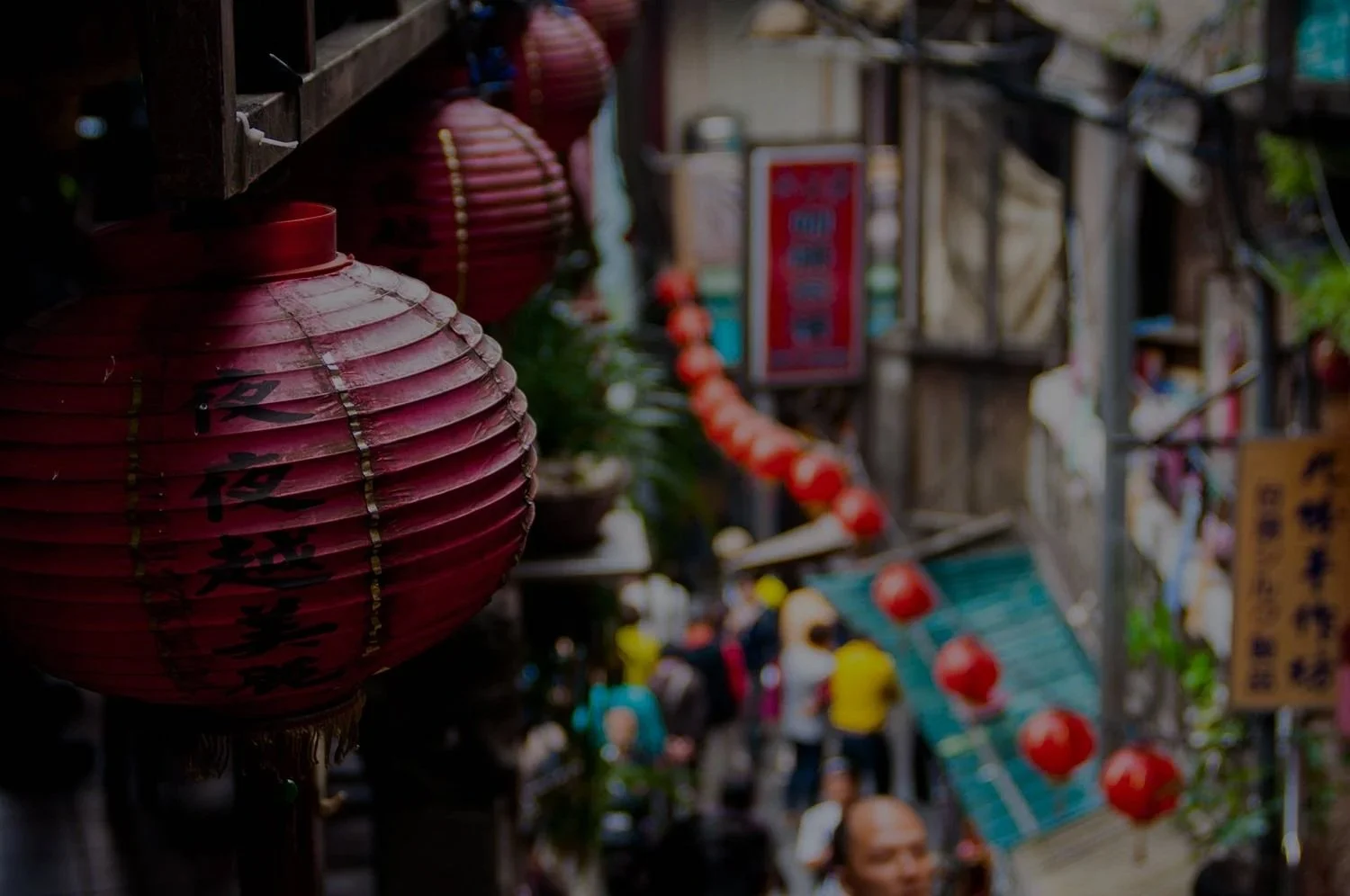 The close up view of Chinese lanterns placed on walls and a blurry view of people walking in a market road in Jiufen Old Street