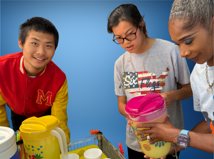 A boy in a wheelchair outdoors in a garden, wearing a navy blue t-shirt, jeans, and red headphones, holding a tablet, with lush greenery and flowers in the background.