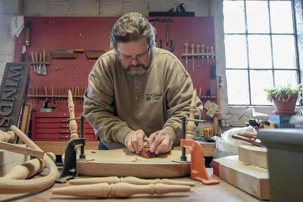 Working inside his shop, Craftsman Garrett Aston shaves down the underside of a Windsor chair, Jan. 10, 2018.Eric Bonzar — The Morning Journal