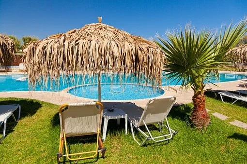 sun loungers and palm leaf umbrella next to a crystal blue swimming pool - ask for what you need when on holiday with a chronic illness