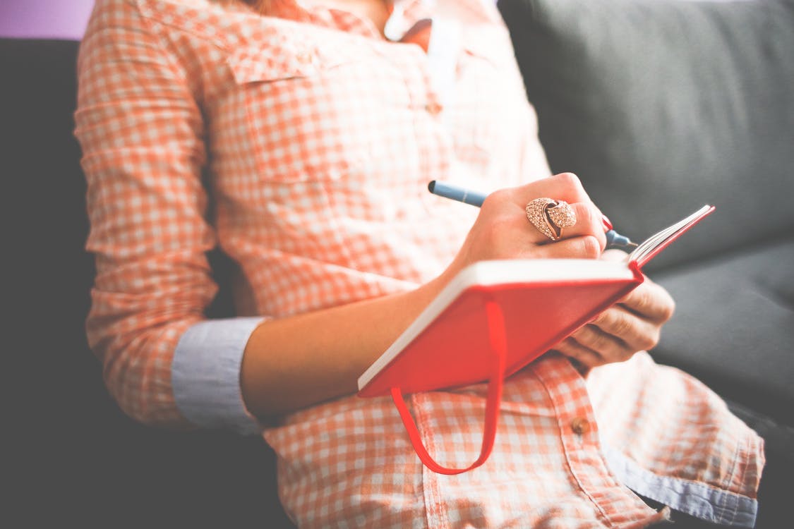 a woman writing in a red journal - Journalling may help to process anxious thought patterns relating to going on holiday with chronic illness