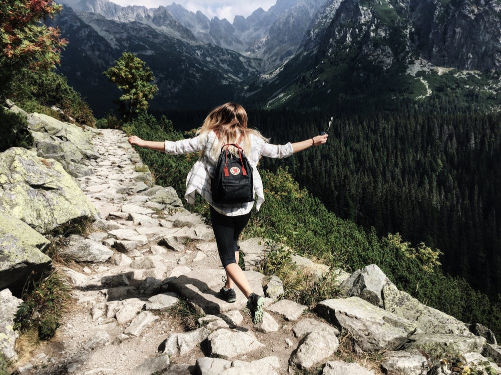 a woman seen from behind hikes along a wall on a hill with arms outstretched with joy - what brings you fulfillment
