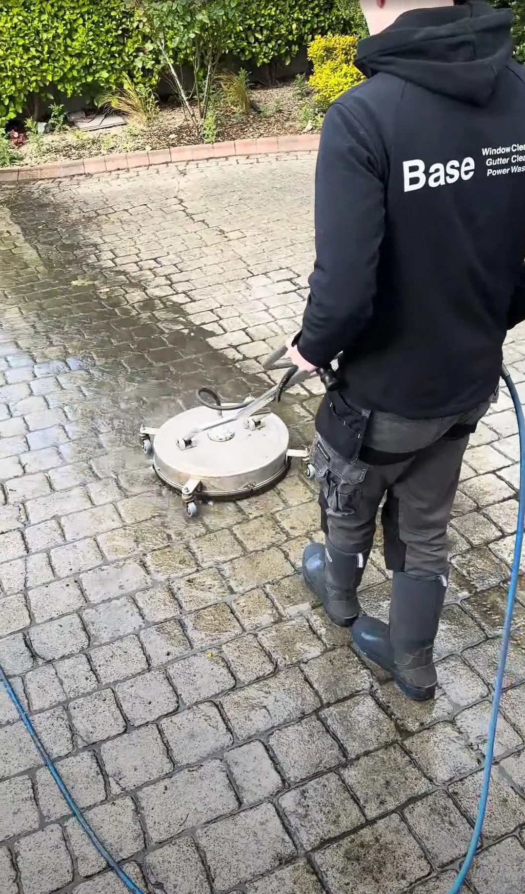 Base team member using professional surface-cleaning equipment to power wash a paved driveway in Dublin.