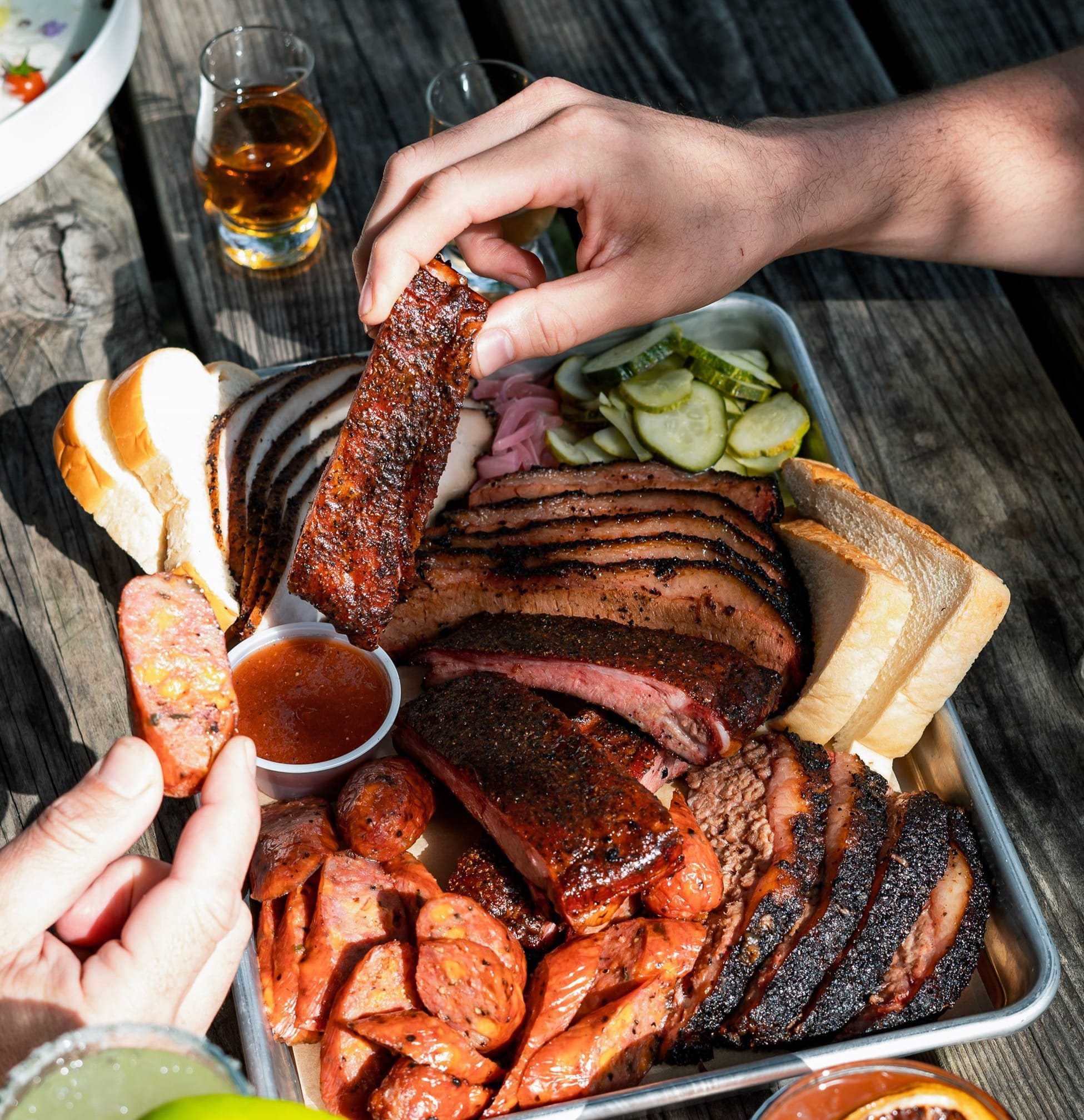 plate of brisket and sausage with side of pickles and bread