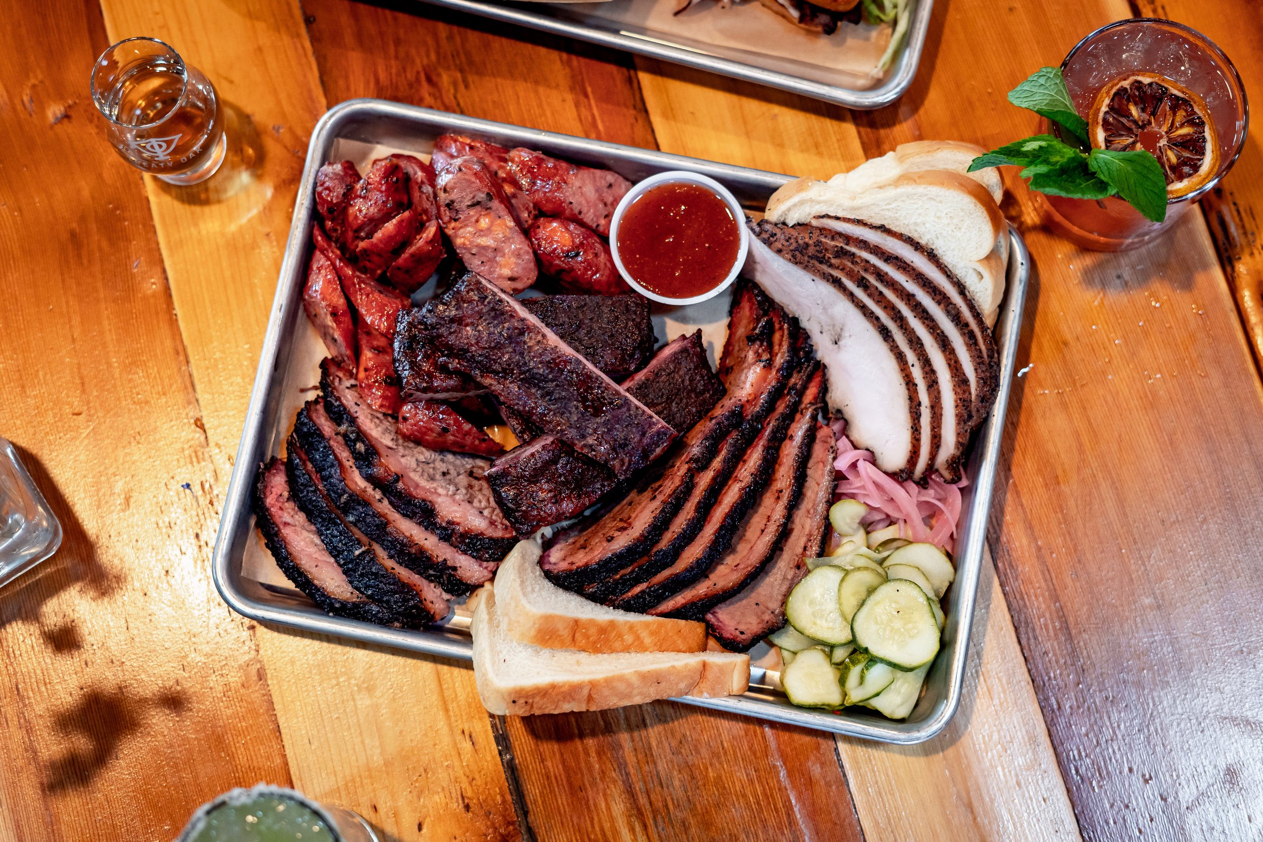 plate of sliced brisket, ham, and sausage with side of pickles and bread