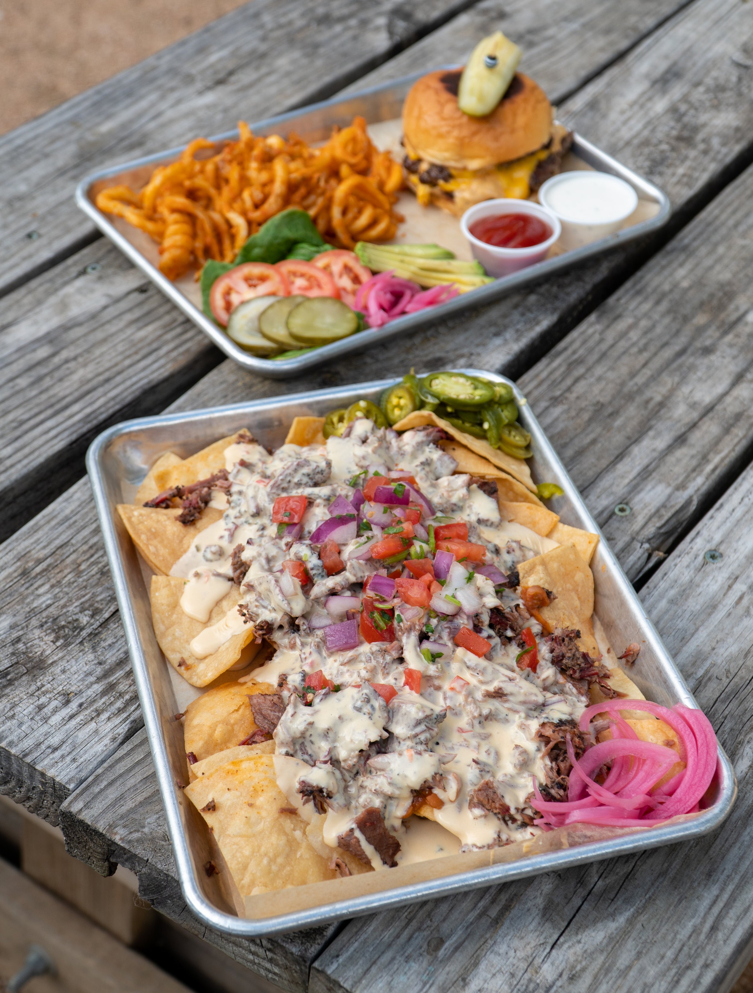 plate of supreme nachos and cheeseburger plate with curly fries in background