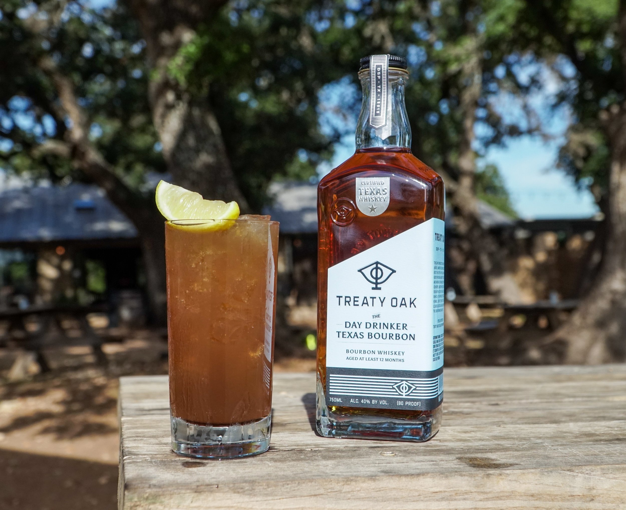 Bottle of Treaty Oak Day Drinker Texas Bourbon and a cocktail next to it on a table