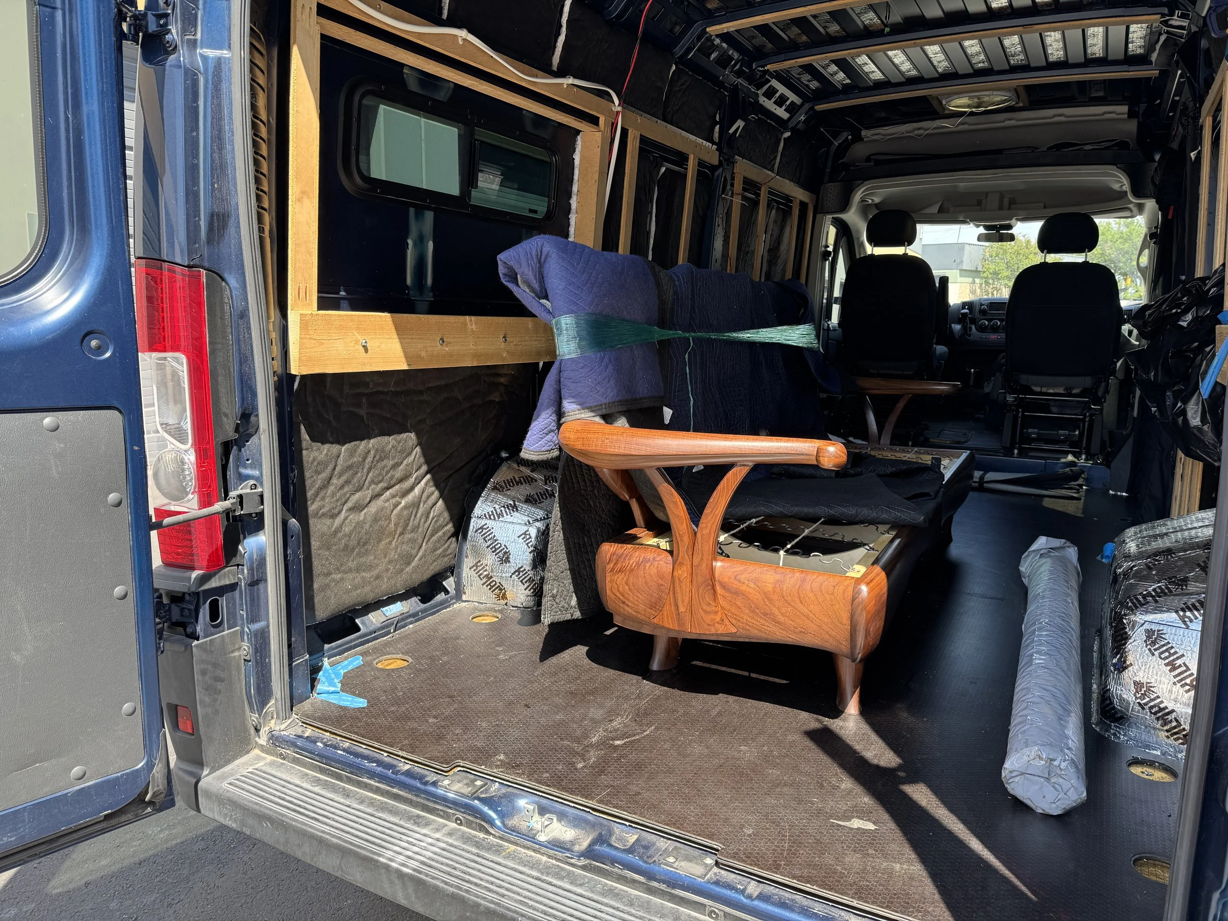 Interior of a van being converted with insulation, wooden framing, and a wooden chair in the center.
