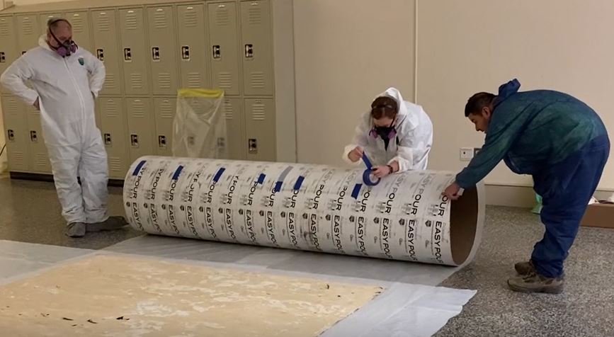  Team puts tape on a large Sonotube in preparation for rolling the mural onto it. 