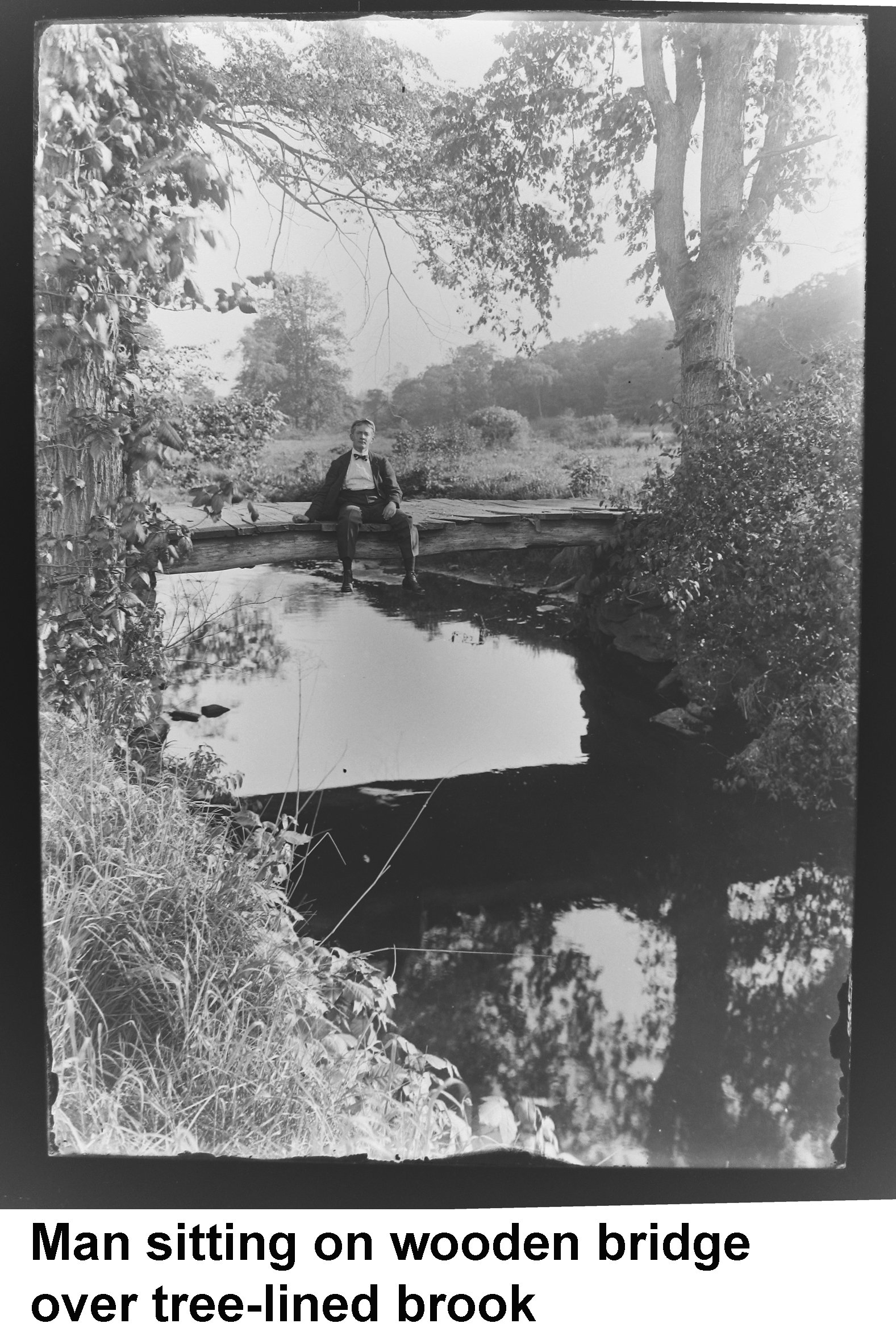 GN-090 Man sitting on wooden bridge over tree-lined brook.jpg