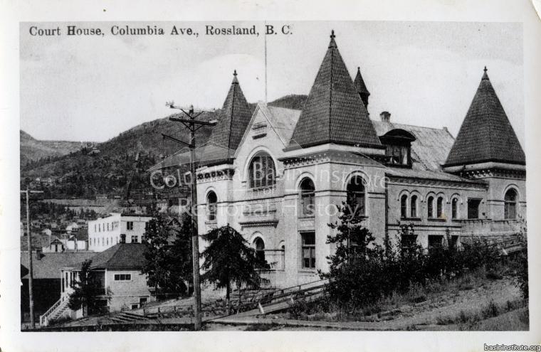 2276.0011 Postcard - Rossland Court House . Notice Landcaster Rooming House  (white) in the background