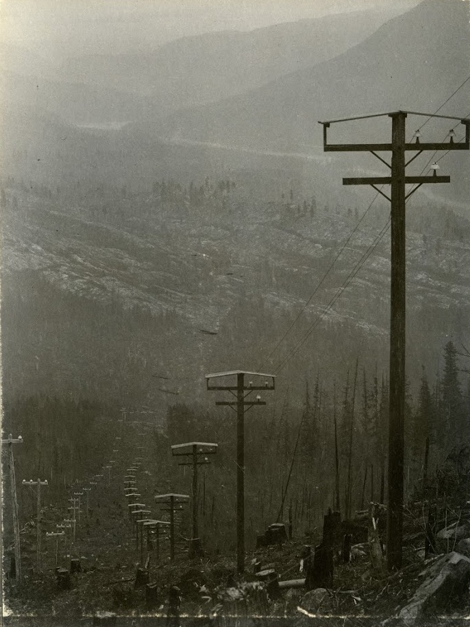 Photo 2348.0048: The first powerlines connecting the Bonnington Plant to Rossland, circa 1898. The roofs seen on top of the lines were specially created for the poles on the Bonnington - Rossland route, as engineers worries the heavy snow loads of the area would interrupt the electrical current if sitting directly on top of the insulators.
