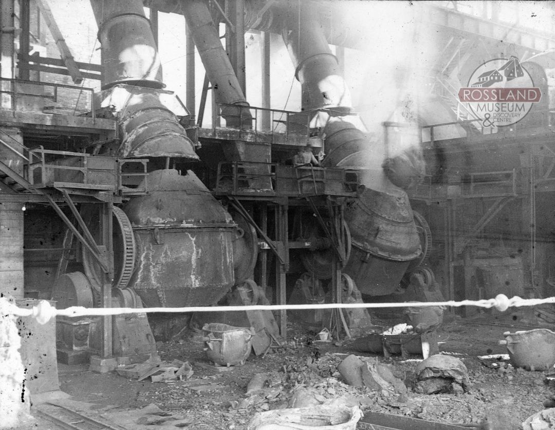 Black and white photograph of two large melting furnaces in an industrial building