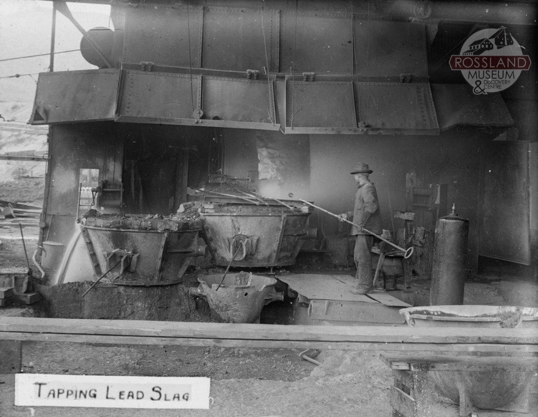 Black and white photograph of man stirring metal in industrial melting pot