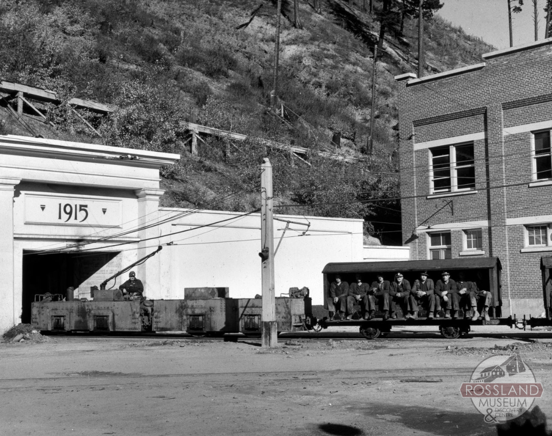 Black and white photograph of a mine locomotive with staff cart about to go into a mine entrance