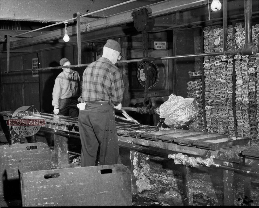 Two male workers working pouring molten metal into molds in an industrial building