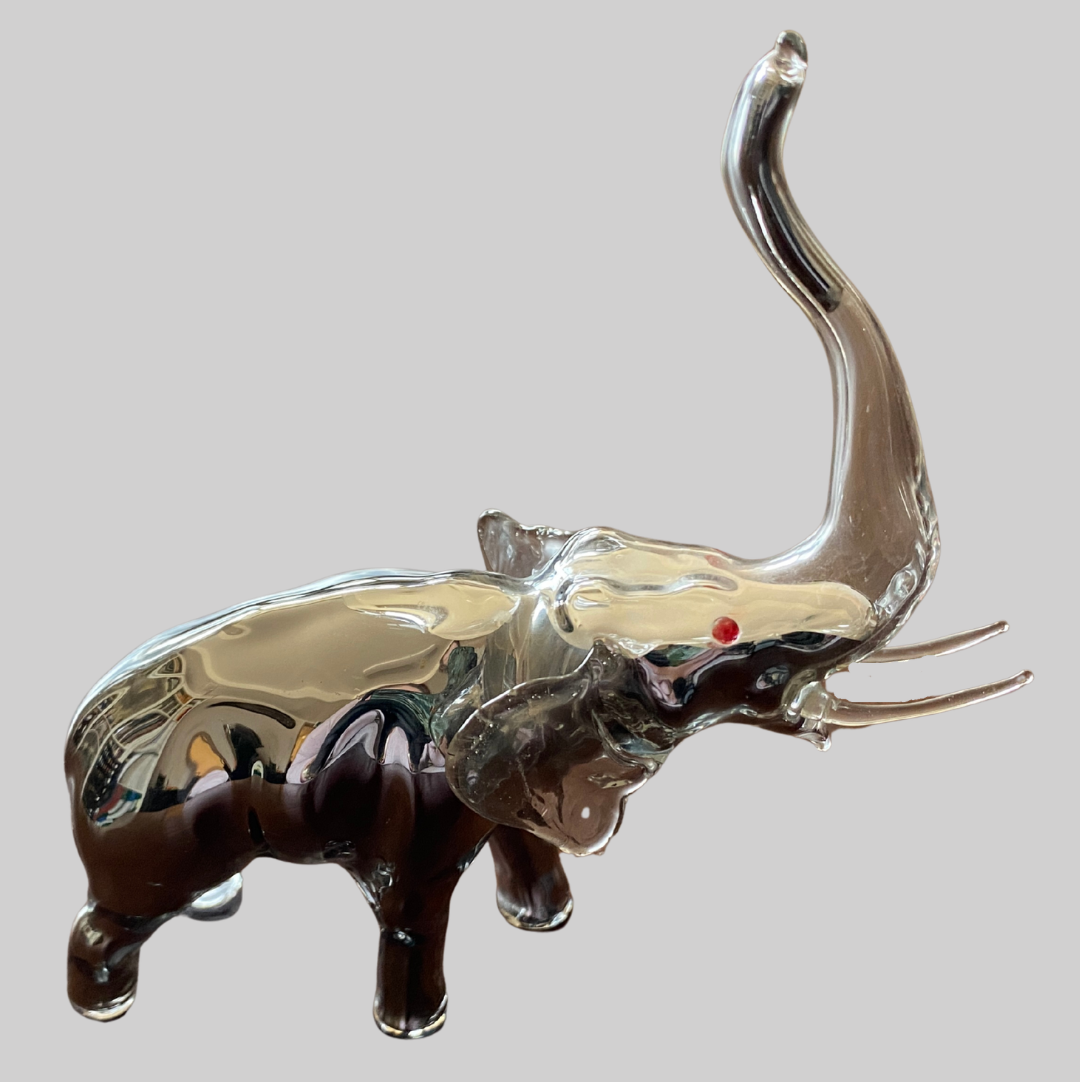 Glass elephant with red eyes that is filled with silver metal on a grey background