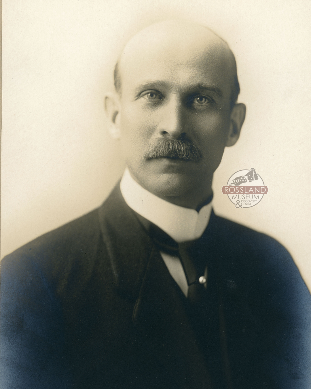 Sepia-toned photograph of balding man wearing black suit