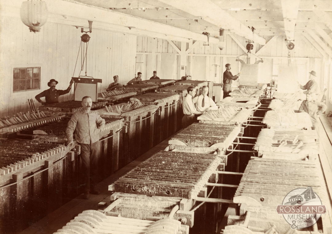 Black and white photograph of several men posed for a photograph inside of an industrial smelting building