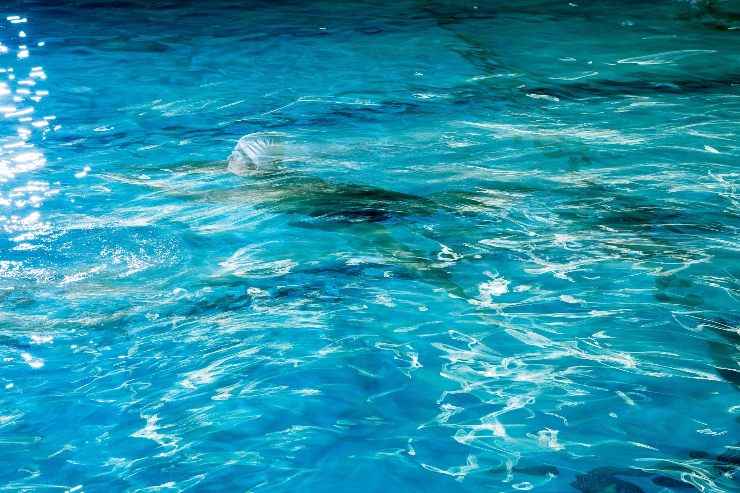 Person swimming underwater in a bright blue pool