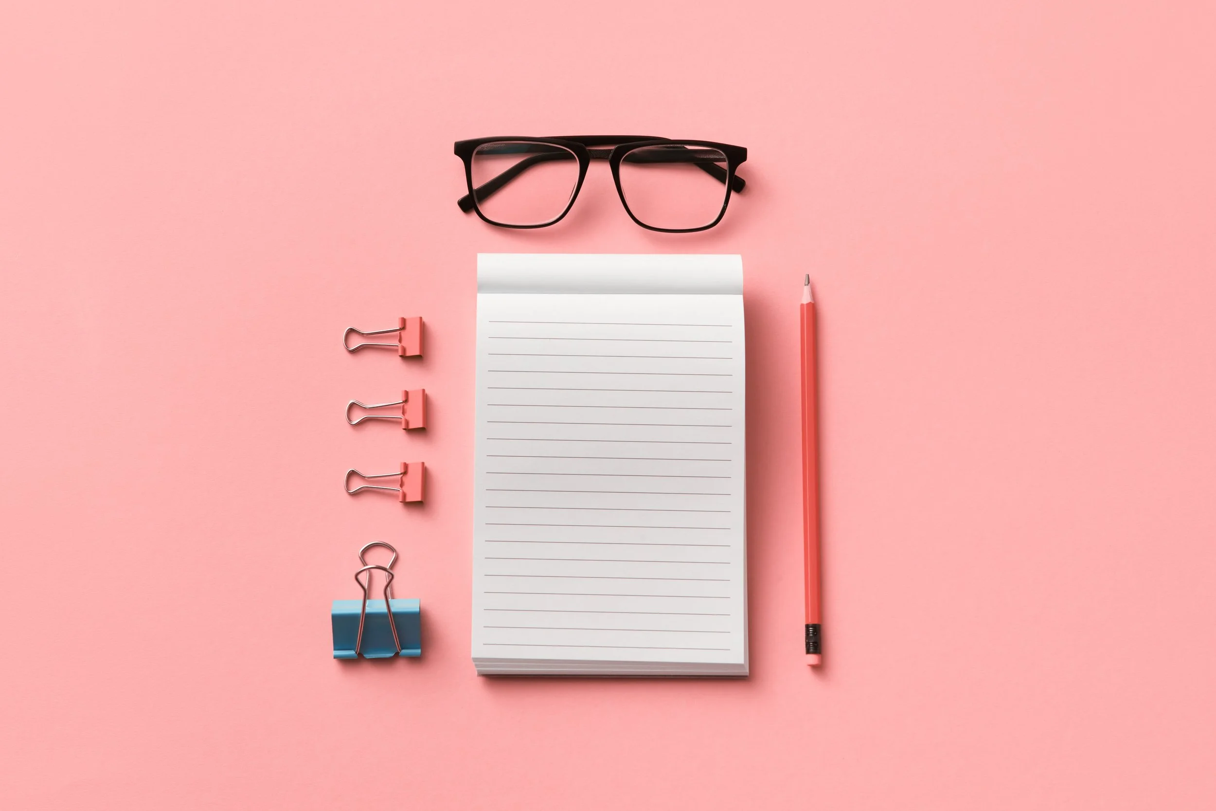 Notepad, pencil, glasses, and binder slips on a pink background